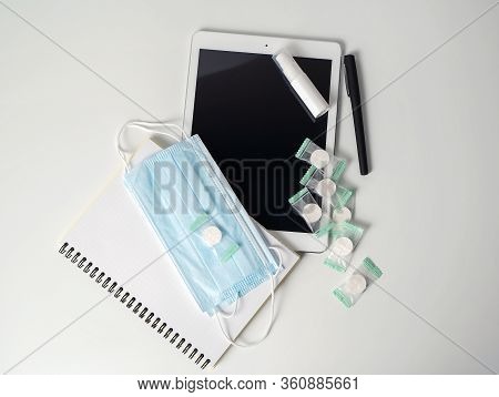 Tablet, Notepad, Pen And Protective Equipment: Alcohol Gel, Napkins, Masks On A White Table. The Con