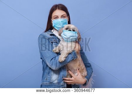 Horizontal Shot Of Young Attractive Lady With Dark Hair Holding Her Little Pet With Protective Mask,