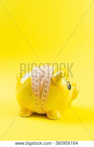 Yellow Piggy Bank In The Form Of A Pig Wrapped With Measuring Tape On A Yellow Background. The Conce