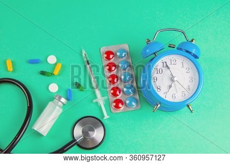 Studio Shot Of Stetoscope, Clock, Syringe And Pills On Light Green Background. Top Views.