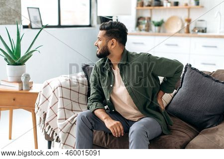 Problems With The Back, Spine, Sciatica. Sad Arabian Or Indian Man, Dressed In Casual Wear, Sitting 