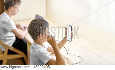 Schoolboys Use Electronic Devices Connected Directly To Head. Younger Brother Connects Cable To Smar