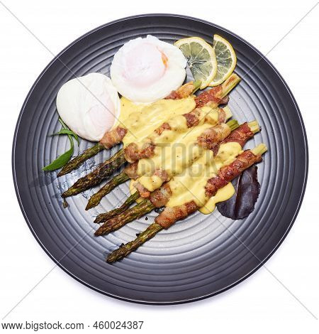Baked Aspargus Covered With Bacon On A Black Ceramic Plate Isolated On White Background