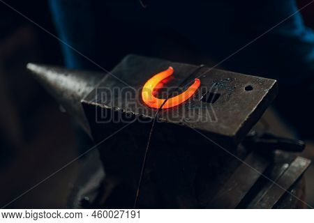 Blacksmith Forges And Making Metal Horseshoe With Hammer And Anvil At Forge.