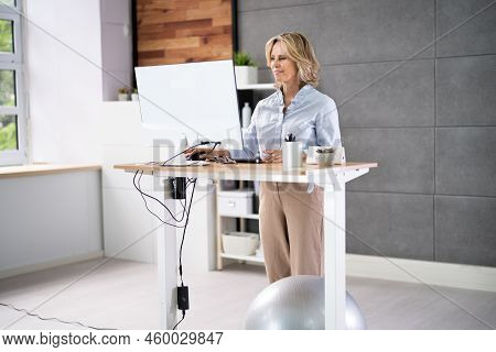 Woman Using Adjustable Height Standing Desk In Office For Good Posture