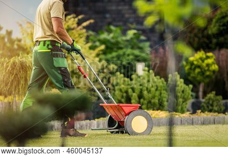 Caucasian Professional Gardener With Push Spreader Fertilizing Residential Lawn For A Good Health An