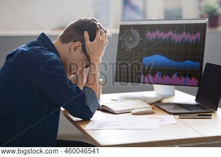 Crypto Crash. Depressed Young Male Employee Sitting At Workplace And Touching Head