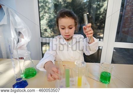 Happy Inspired European Preschooler Girl In White Lab Coat Pours And Combines Chemicals During Scien