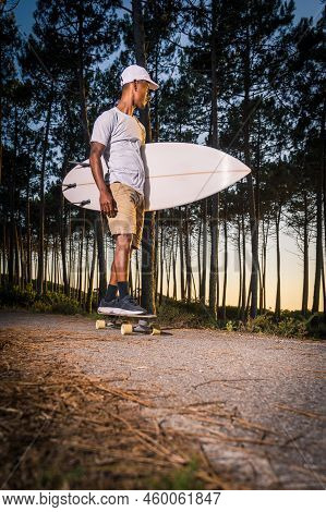 Surf Skater Rolling By The Pine Forest At Sunset With His Surfboard In Maceda, Ovar - Portugal.