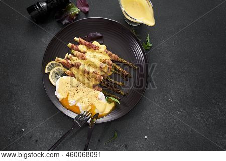 Baked Aspargus Covered With Bacon And Poached Eggs On A Black Ceramic Plate