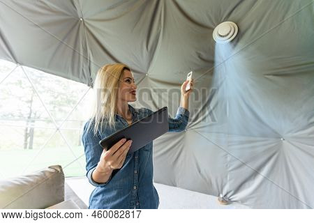 Woman With Tablet Turning On Ventilation System As A Recuperator For Fresh Indoor Air Quality, Smart