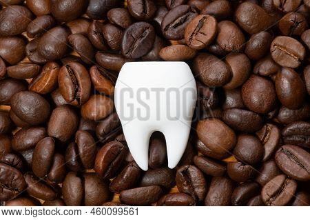 Large White Tooth On A Pile Of Roasted Coffee Beans. Coffee Staining And Teeth Whitening Concept.