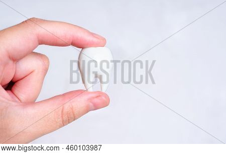 Hand Pinch-holding A Large White Tooth Isolated On A Neutral Background With Copy Space. Teeth Care 