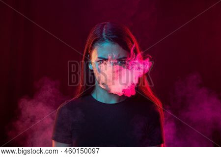 Angry Young Girl With Dark Hair Releases Smoke From The Mouth Isolated Over Pink Background. Concept