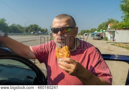 Portrait Of Hungry Ukrainian Senior Driver Taking Patty Near His Car While Standing Near Vasylivka, 