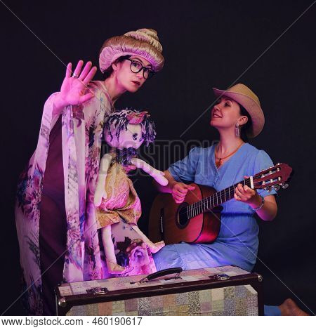 Happy Women In Funny Wigs Give A Musical Performance On A Studio Black Background. Smiling Women Sho