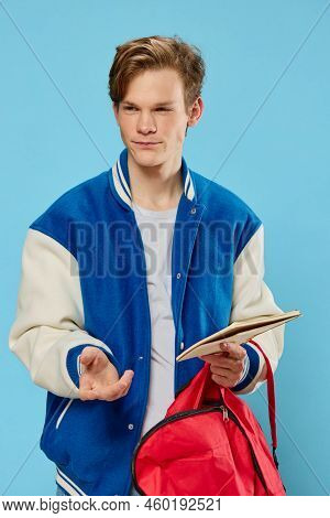 A Pensive Student In A Blue Stylish Bomber Jacket Stands With A Notebook In His Hands And Looks Away