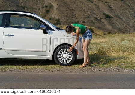 Lady Driver Checks Tires On Wheel Of White Vehicle Parked On Roadside Of Highway In Rural Area. Youn