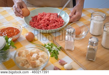 Woman's Hands Preparing  Meatballs With Raw Materials To Mix, Home Kitchen And Yellow Tablecloth