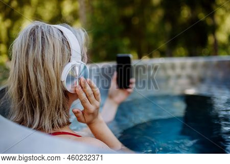 Reaxed Woman With Headphones Listening To Music In Outdoor Bathtub, Rear View.