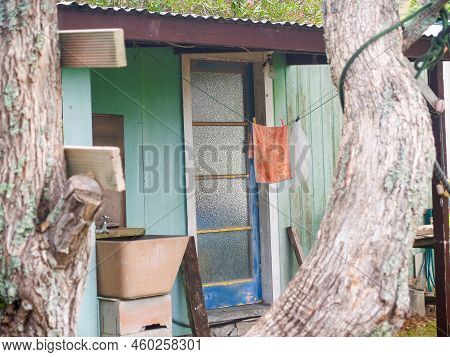 Rustic Exterior To Small Accommodation Building With Orange Towel Hanging With Closed Door.