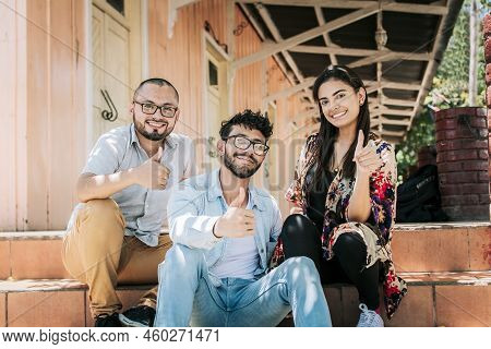 Group Of Happy Friends Sitting On The Stairs Giving Thumbs Up. Portrait Of Happy Teenagers Sitting O
