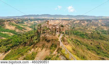 A Tiny Italian Town Stands On A High Cliff With A Long Bridge To It, Surrounded By Vegetation, Field