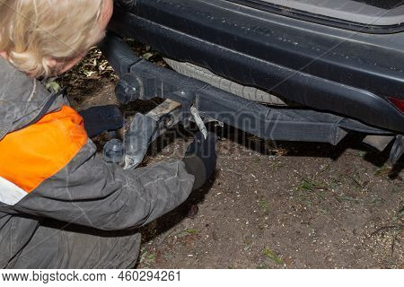 A Man Mounts The Hook Of An Iron Towbar On A Car For Towing A Trailer. Device For Transportation.