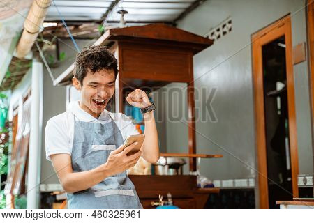 Happy Male Merchant Wearing Apron Looking At Mobile Phone Screen