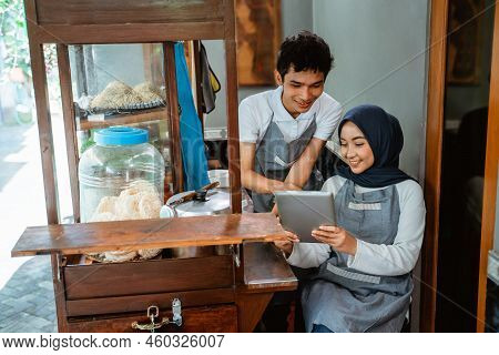 Two Sellers Wearing Aprons Using Pads When Selling Chicken Noodles