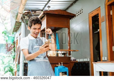 Excited Male Salesman Wearing Apron When Looking At Mobile Phone