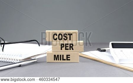 Cost Per Mile Text On A Wooden Block With Notebook,chart And Calculator, Grey Background