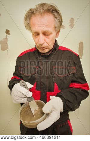 Older Man Working In Empty Apartment Repairing Holes In Walls
