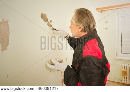 Older Man Working In Empty Apartment Repairing Holes In Walls
