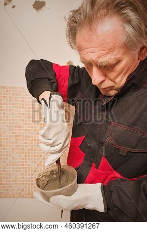 Older Man Working In Empty Apartment Repairing Holes In Walls