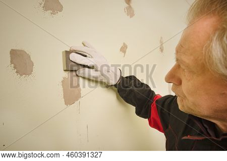 Older Man Working In Empty Apartment Sanding Repair Walls Before Painting