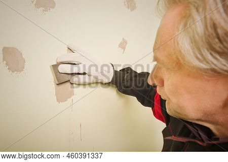 Older Man Working In Empty Apartment Sanding Repair Walls Before Painting