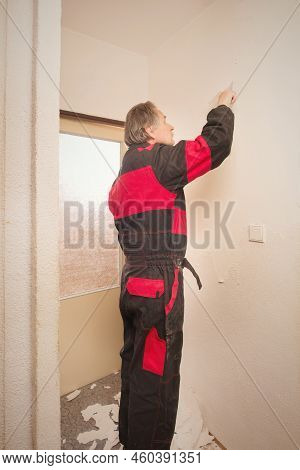 Older Man Removing Old Wallpapers Off The Walls In Empty Apartment