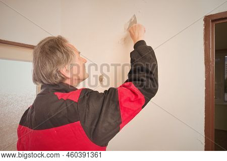 Older Man Removing Old Wallpapers Off The Walls In Empty Apartment