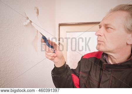 Older Man Removing Old Wallpapers Off The Walls In Empty Apartment