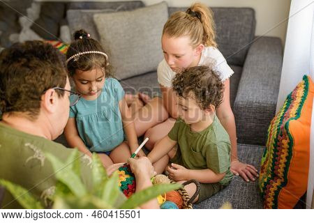 Senior Woman Spending Day With Her Grandchildren, Knitting Granny Square At Home. Two Girls, Grandmo