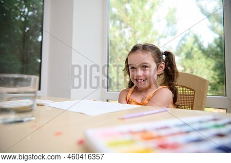 Caucasian Cute Funny Little Girl Of Preschool Age, Cutely Smiles, Looking At The Camera While Learni