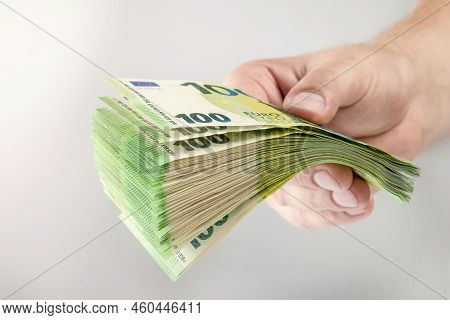 Large Stack Of Euros In Hand. Banknotes Of 100 Euros In A Male Hand On A Uniform Background. A Man H