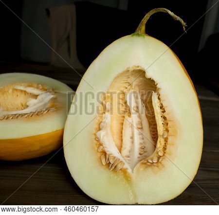 Half A Melon On The Table. Vertical Photo, Dark Background And Light Melon Flesh. Two Halves Of A Me