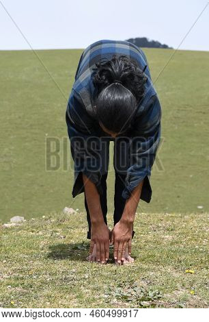 A Long Haired Young Man Doing Warm Up By Uttanasana Yoga Pose (standing Toe Touch) Stretch Exercise 