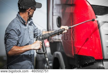 Caucasian Semi Truck Driver Washing His Vehicle Using Pressure Washer And Cleaning Detergent. Trucks