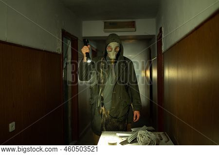 Man In Respirator Gas Mask With Flashlight Inside Of Abandoned Building In Dark. Cyberpunk Postapoca