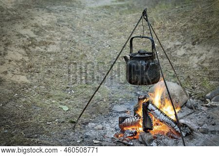 Campfire With Cooking Food In A Saucepan On A Tripod. Cooking On Fire, Camping Cooking. Living In Te