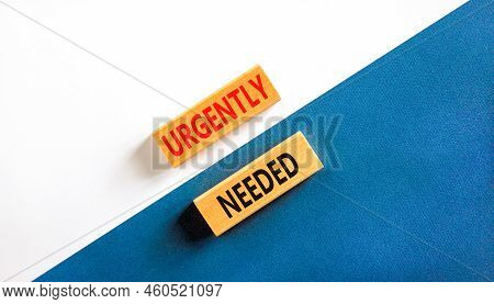 Urgently Needed Symbol. Concept Words Urgently Needed On Wooden Blocks On A Beautiful White And Blue