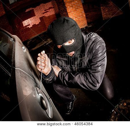 Røver og biltyv i en maske åbner døren til bilen og kaprer bilen.